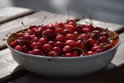 A ceramic bowl filled with fresh red cherries on an outdoor wooden table. Perfect summer fruit.