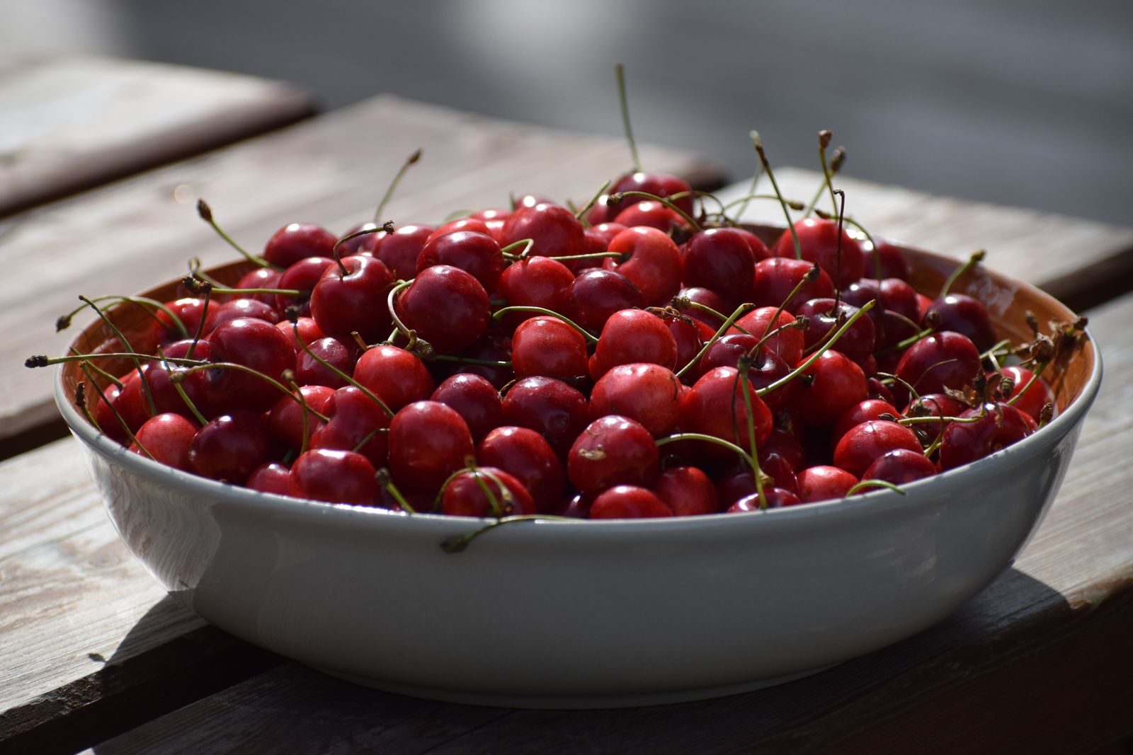 A ceramic bowl filled with fresh red cherries on an outdoor wooden table. Perfect summer fruit.