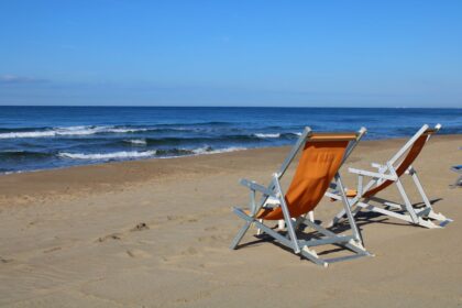 Two empty deck chairs on a sandy beach under clear blue skies in Latina, Italy.
