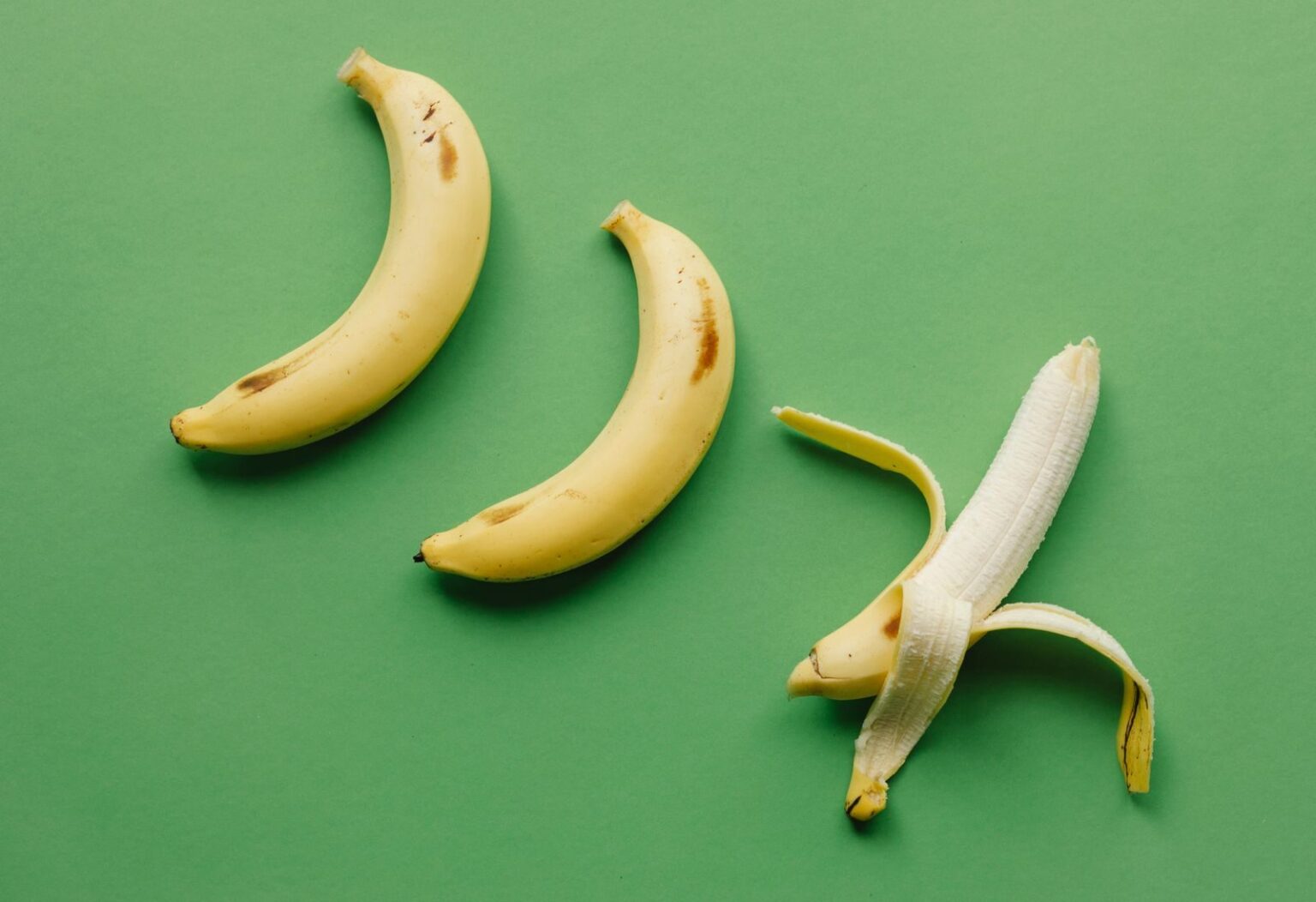 High angle of fresh ripe sweet peeled banana on green background with unpeeled bananas