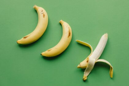High angle of fresh ripe sweet peeled banana on green background with unpeeled bananas