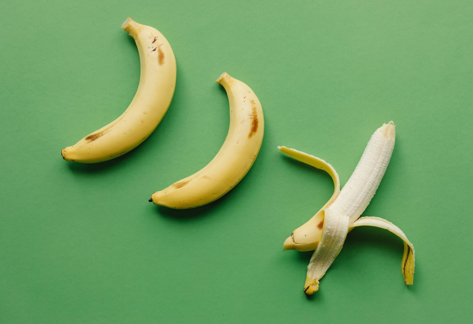 High angle of fresh ripe sweet peeled banana on green background with unpeeled bananas