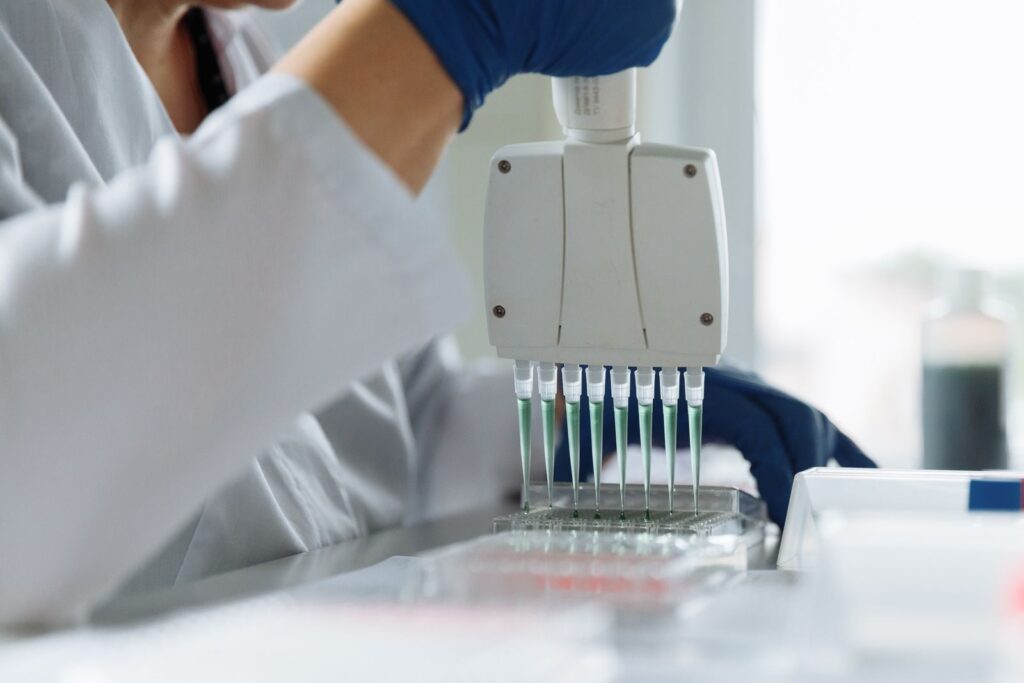 A scientist wearing a lab coat uses a multichannel pipette for liquid handling in a lab setting.