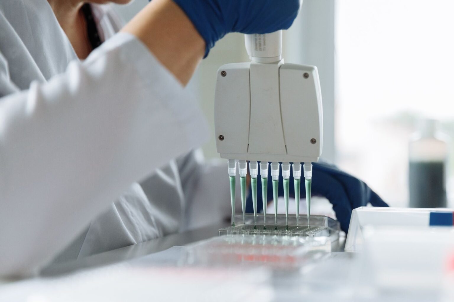 A scientist wearing a lab coat uses a multichannel pipette for liquid handling in a lab setting.